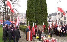 Przy pomniku niepodległości stoją poczty sztandarowe. Przy mikrofonie głos zabiera dyrektor Domu Kultury we Włoszczowie.