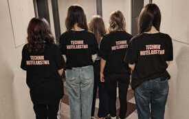 Pięć uczennic stoi tyłem prezentując napis na swoich koszulkach: technik hotelarstwa