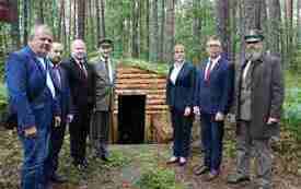 Uczestnicy uroczystości na tle ziemnego bunkra partyzanckiego.