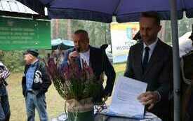 Prowadzący uroczystość wraz z przemawiającym gościem. Na pierwszym planie wrzos. 