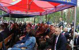 Uczestnicy uroczystości siedzą pod namiotem.