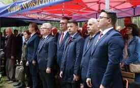 Uczestnicy uroczystości stoją pod namiotem.