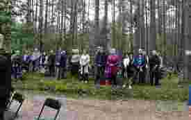 Uczestnicy uroczystości stoją na skraju lasu.