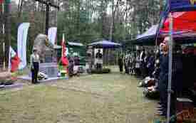 Po lewej stronie warta honorowa harcerzy przy obelisku , po prawej pod namiotami siedzą uczestnicy uroczystości.