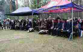 Pod namiotami siedzą zaproszeni goście i uczestnicy uroczystości patriotycznej.