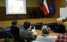 Studenci siedzą przy stołach w sali konferencyjnej. Wykład prowadzi dr Anna Szczukocka