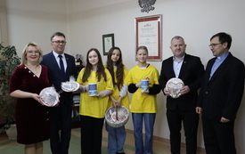 W gabinecie starosty stoją członkowie Zarządu trzymając ciasteczka w kształcie serca. W środku w ż&oacute;łtych podkoszulkach uczniowie ze szkoły w Olesznie.