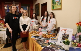 Stoisko promocyjne szkoły. Za stołem stoją uczniowie prezentujący prace kulinarne.