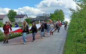 Uczestnicy uroczystości maszerują ulicami miasta. Dzieci z Oleszna niosą dużą flagę Polski.