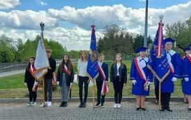 Poczty sztandarowe stoją w szeregu na placu przed pomnikiem