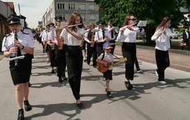 Orkiestra i pozostali uczestnicy uroczystości maszerują sprzed Urzędu Gminy do kościoła