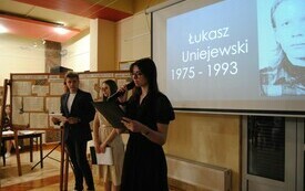 Prowadzący uroczystość na scenie konferansjerzy. W tle slajd z nazwą konkursu i portretem patrona.