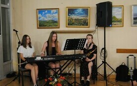 Występ zespołu muzycznego. Trzy dziewczyny siedzą z instrumentami muzycznymi.