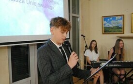 Uczeń na scenie odczytuje wiersz do mikrofonu.