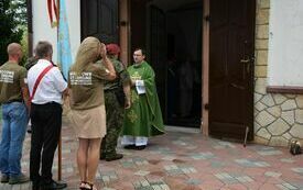 Ksiądz stoi w progu kościoła i zaprasza uczestnik&oacute;w uroczystości na mszę