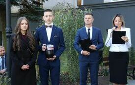 Uczeń z uczennicą trzymają w rękach kapsułę czasu, obok stoi dw&oacute;jka nauczycieli opowiadających co znalazło się w kapsule