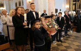Dzieci, młodzież, rodzice i nauczyciele stoją w kolejce by złożyć dary ołtarza