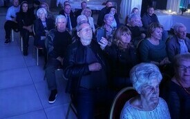 Publiczność siedzi na krzesłach przed sceną i ogląda koncert