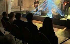 Zesp&oacute;ł występuje na scenie, przed sceną na krzesłach siedzi publiczność