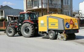 Traktor z urządzeniem do zamiatania jedzie ulicą Ogrodową