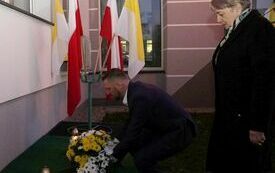 Dyrektor ZOZ składa wiązankę kwiat&oacute;w przed tablicą poświęconą Janowi Pawłowi II, kt&oacute;ra wisi na ścianie szpitala