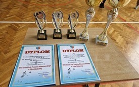 Na stoliku leżą przygotowane dla drużyn puchary i dyplomy
