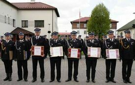 W szeregu stoją strażacy prezentując otrzymane dyplomy oprawione w ramkę