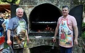 Wiceprzewodniczący Rady Powiatu i Radny powiatowy stoją w fartuszkach przy grillu, na kt&oacute;rym smażą kiełbasy i kaszanki