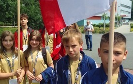 Uczniowie uczestniczą w prezentacji drużyn. W rękach trzymają tabliczkę z nazwą: wojew&oacute;dztwo świętokrzyskie